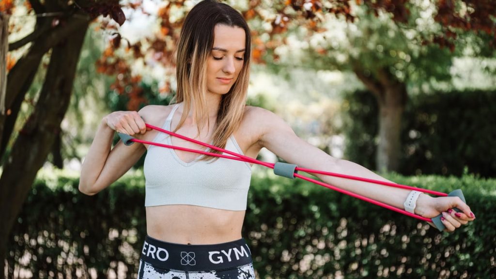 Fit woman using a resistance band for exercise in a sunny outdoor setting.