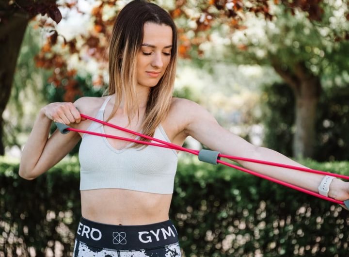 Fit woman using a resistance band for exercise in a sunny outdoor setting.
